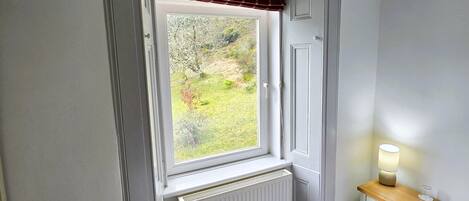 A bedroom with a window, radiator, bedside table with a lamp, and a bed.