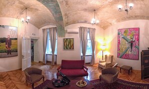 A spacious room with a red sofa, two armchairs, a wooden floor, and a large painting on the wall. - Zagreb Speeka Hostel (Zagreb)
