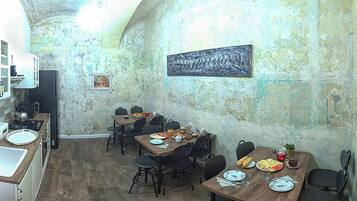 Un comedor rústico con mesas y sillas de madera, una cocina con lavamanos y estufa, y una pared de textura rugosa con un cuadro de un tiburón.