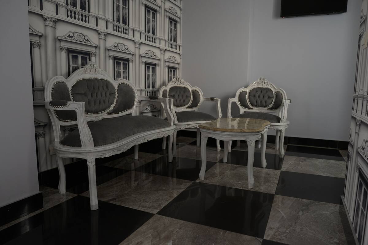 Een kamer met een zwart-wit geruit vloertje, twee sierlijke witte stoelen met beklede zitplaatsen, een klein rond tafeltje en een wandgemonteerde flatscreen televisie.