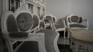 Een kamer met gedetailleerd, antiek meubilair, waaronder een stoel met een hoge rugleuning en decoratieve details, en een tafel met een marmeren blad.