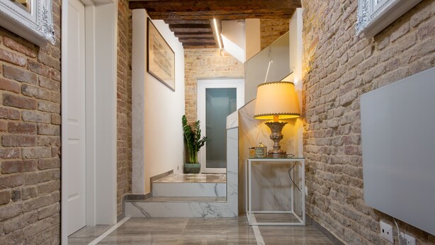 A hallway with exposed brick walls, a marble floor, and a staircase leading to another room. - Cà Patron (Venice)