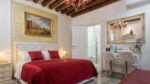 A bedroom with a large bed, a desk, two chairs, a mirror, and a chandelier. - Cà Patron (Venice)