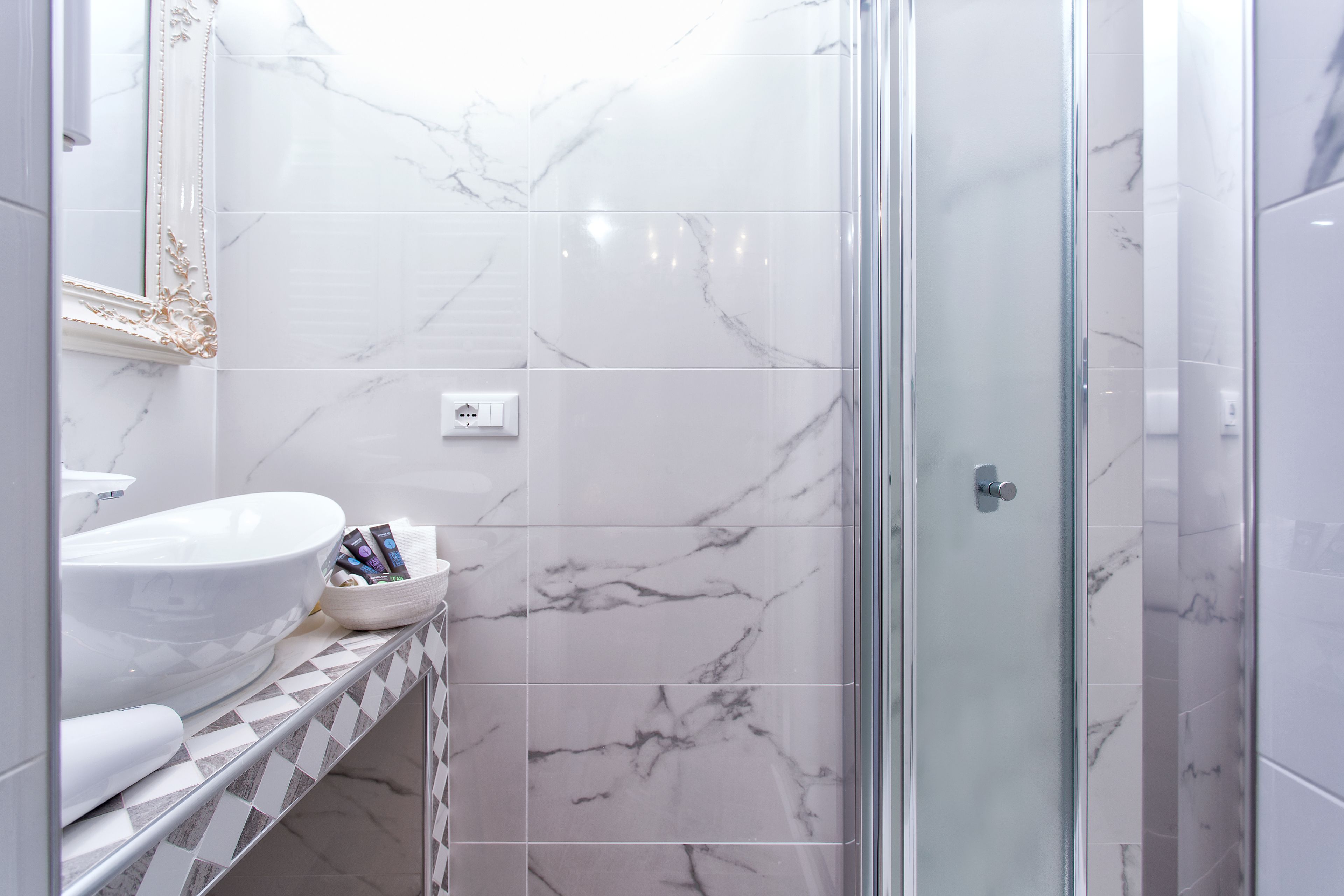 A bathroom with a white marble sink, a glass shower enclosure, and a tiled floor.