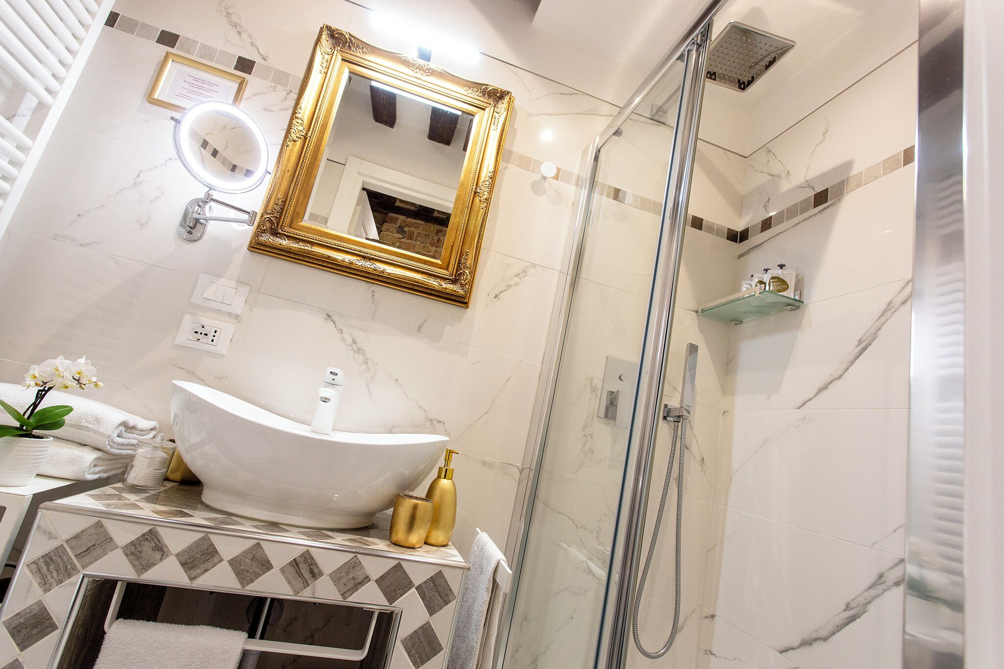 A bathroom with a white sink, gold fixtures, a large mirror, and a glass shower enclosure.