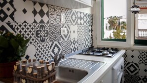 A kitchen with patterned tiles, a gas stove, and a window with a view of palm trees. - Domus Linda B&B (Forio)