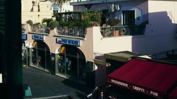 A view of a coastal town with buildings, a mountain in the background, and a red awning with the text "SPIZIOSERIE - CREPES - PUB". - Domus Linda B&B (Forio)