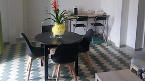 A dining area with a round table, black chairs, and a potted plant. There is a kitchen area with a counter and chairs in the background. - Domus Linda B&B (Forio)