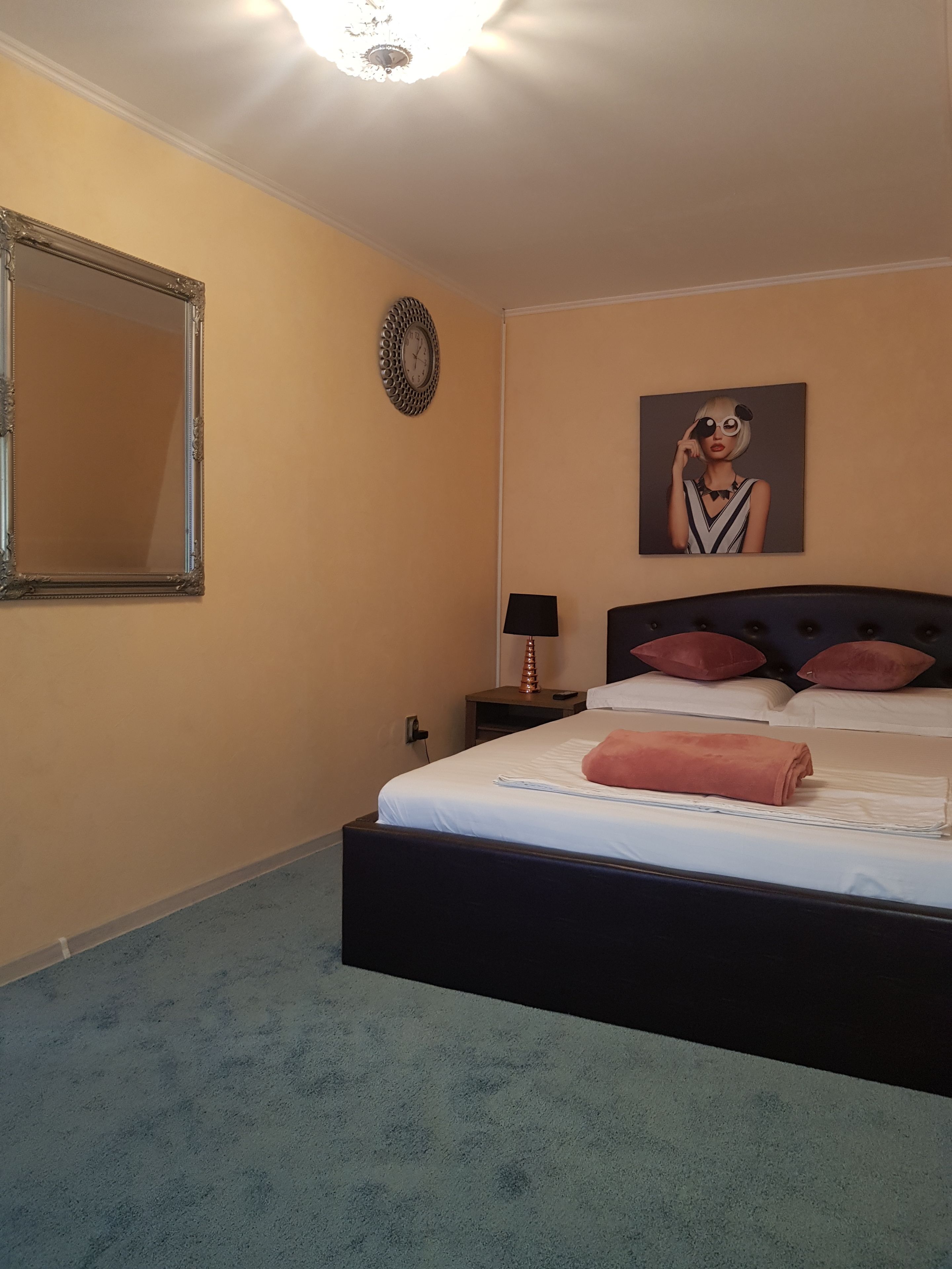 Una cama bien hecha con un cabecero negro, un reloj de pared y un cuadro colgado encima.