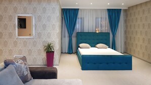A modern bedroom with a large bed, a sofa, a potted plant, and a mirror on the wall. - Art Boutique Central (Tirgu Jiu)