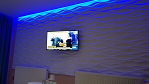 A modern living room with a flat-screen TV mounted on a textured wall, a small round table with a lamp, and a radiator. - Art Boutique Central (Tirgu Jiu)