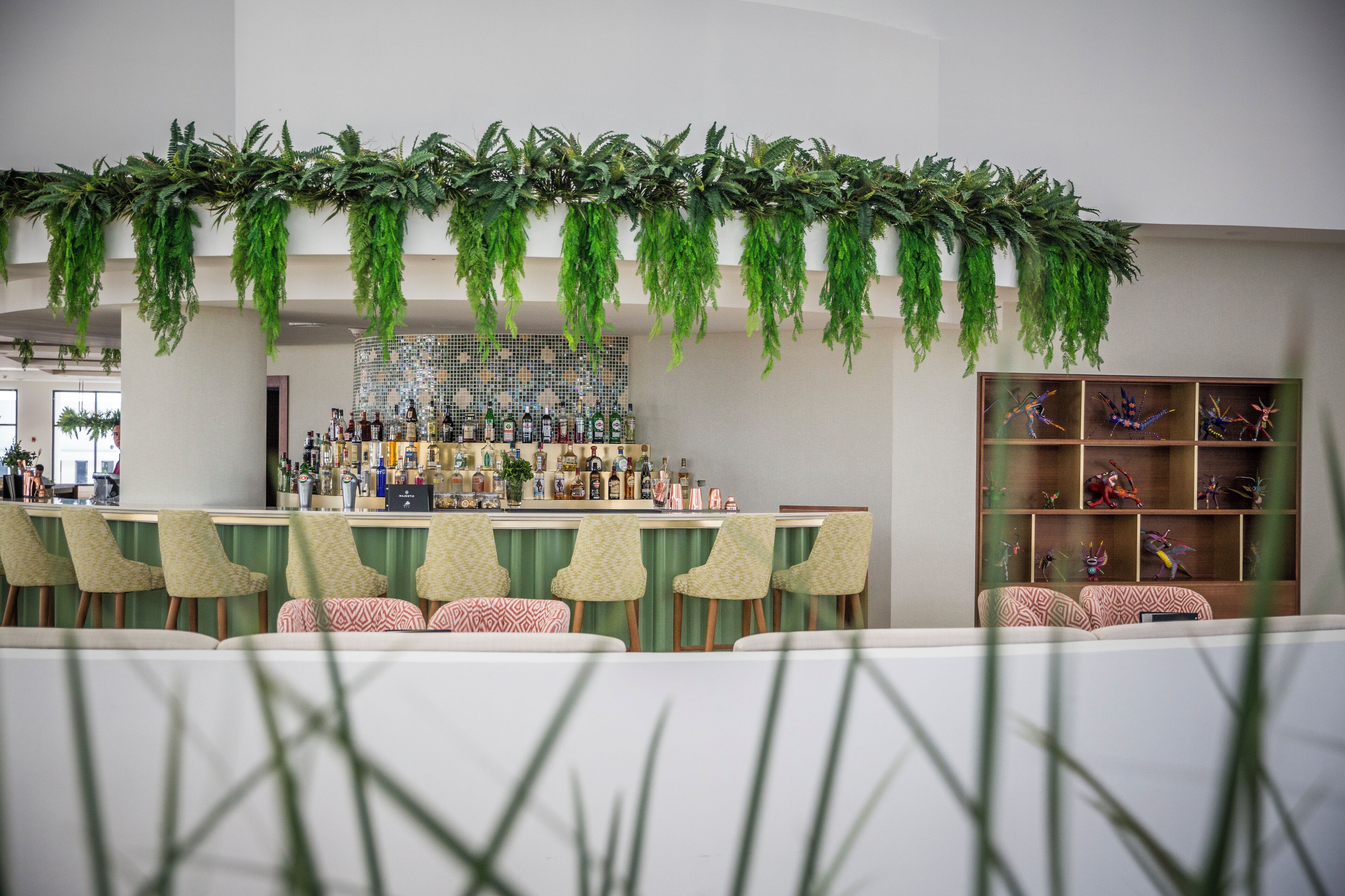 A bar area with hanging greenery, a bar counter, and shelves with bottles.