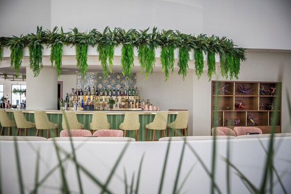 Una zona de bar con follaje colgante, una barra y estanterías con botellas.