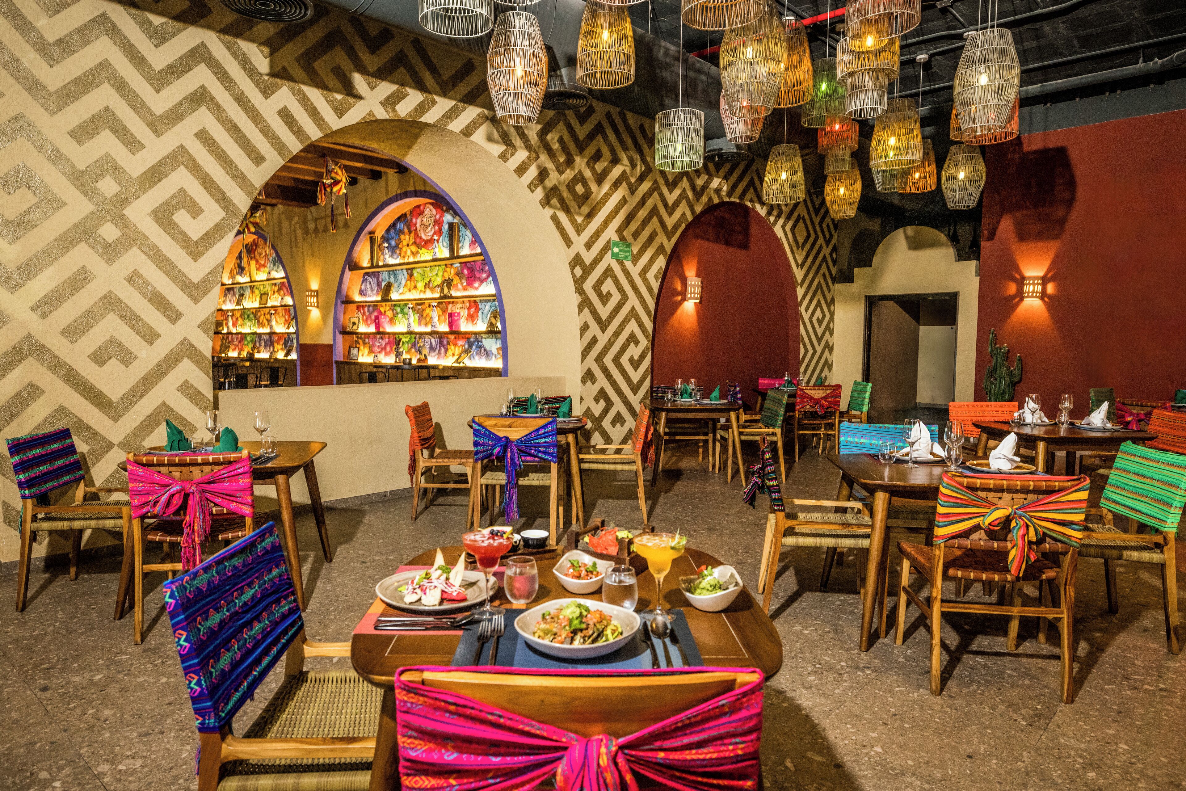 A restaurant with wooden tables and chairs, colorful bow ties on the chairs, and hanging light fixtures.