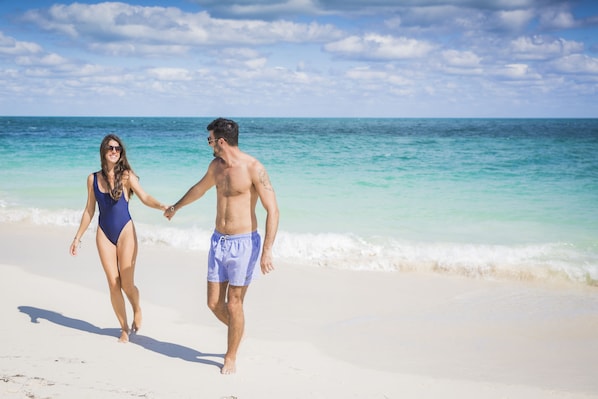 Una pareja caminando sobre una playa con cielos despejados y aguas tranquilas.
