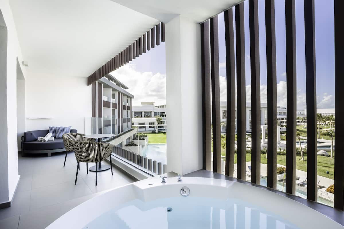 A modern balcony with a large bathtub, a sofa, and a dining table.