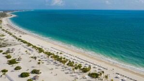 A beach with clear turquoise waters, white sand, and rows of beach umbrellas and lounge chairs. - Majestic Elegance Costa Mujeres – All Inclusive (Costa Mujeres)