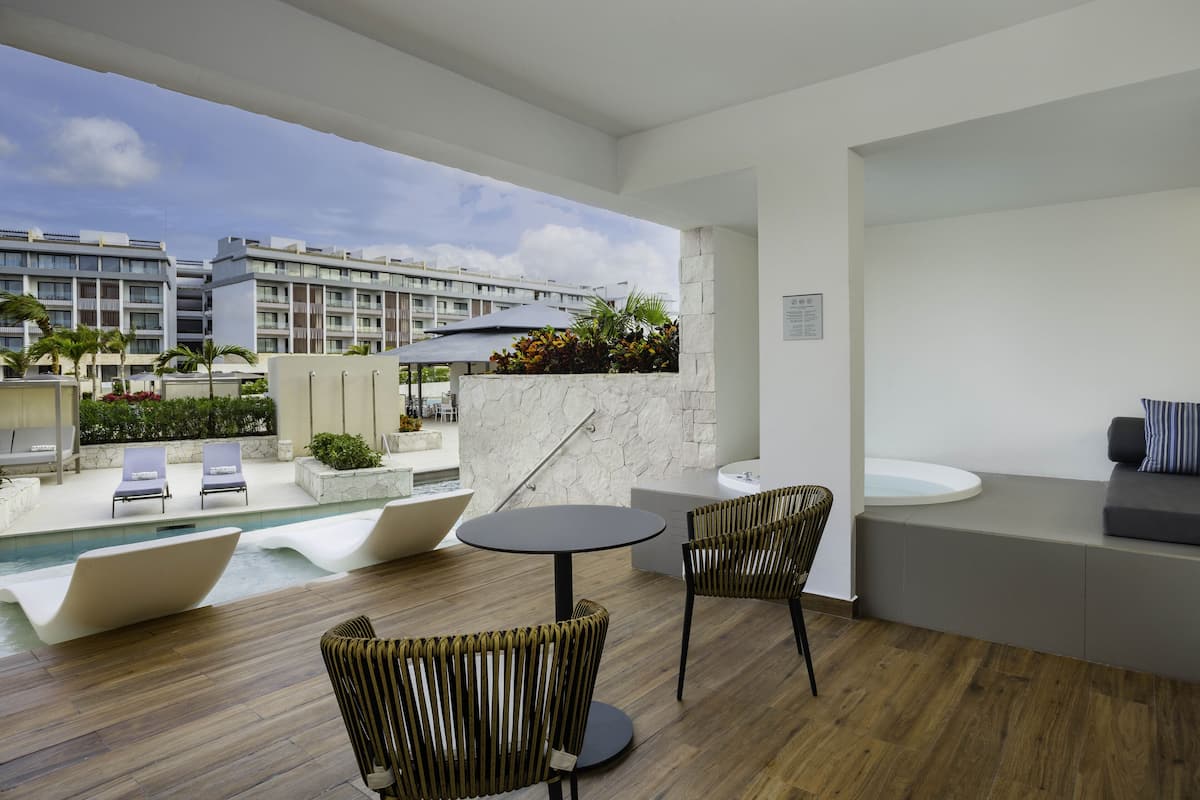 A modern indoor pool area with lounge chairs, a round table, and a seating area with a sofa.