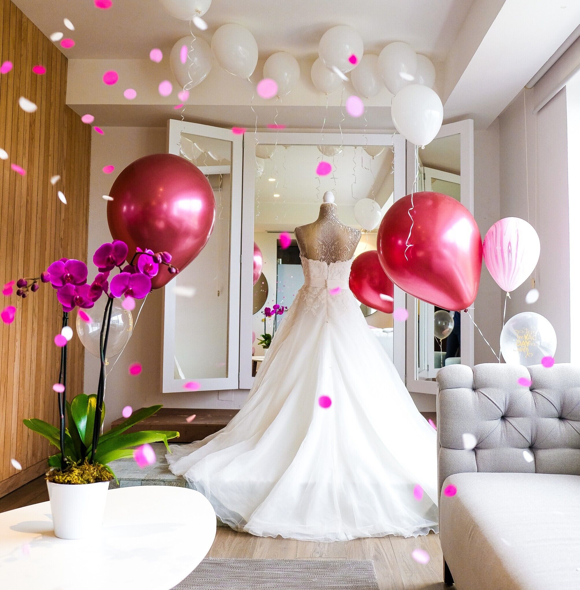 Una habitación con un maniquí vestido de novia, globos y una orquídea en maceta.
