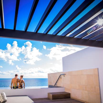 A modern room with a view of the sea, a sunlit ceiling, and a stone wall.