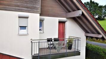 Ein Wohngebäude mit Balkon, roter Tür und Fenster mit weißem Rollo.