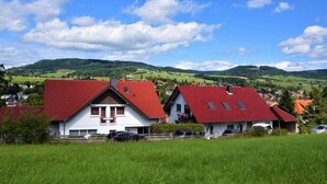A rural village with houses having red roofs, surrounded by green fields and hills. - Gästehaus Jäger (Gersfeld)