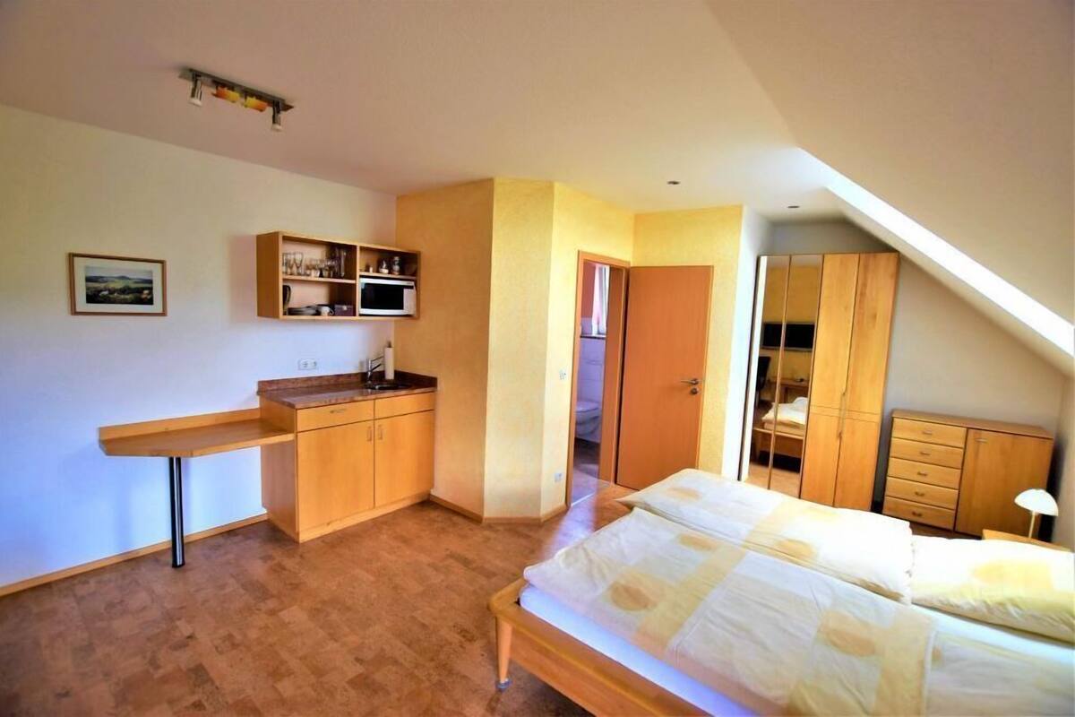 A bedroom with a bed, wooden wardrobe, and a small kitchenette.