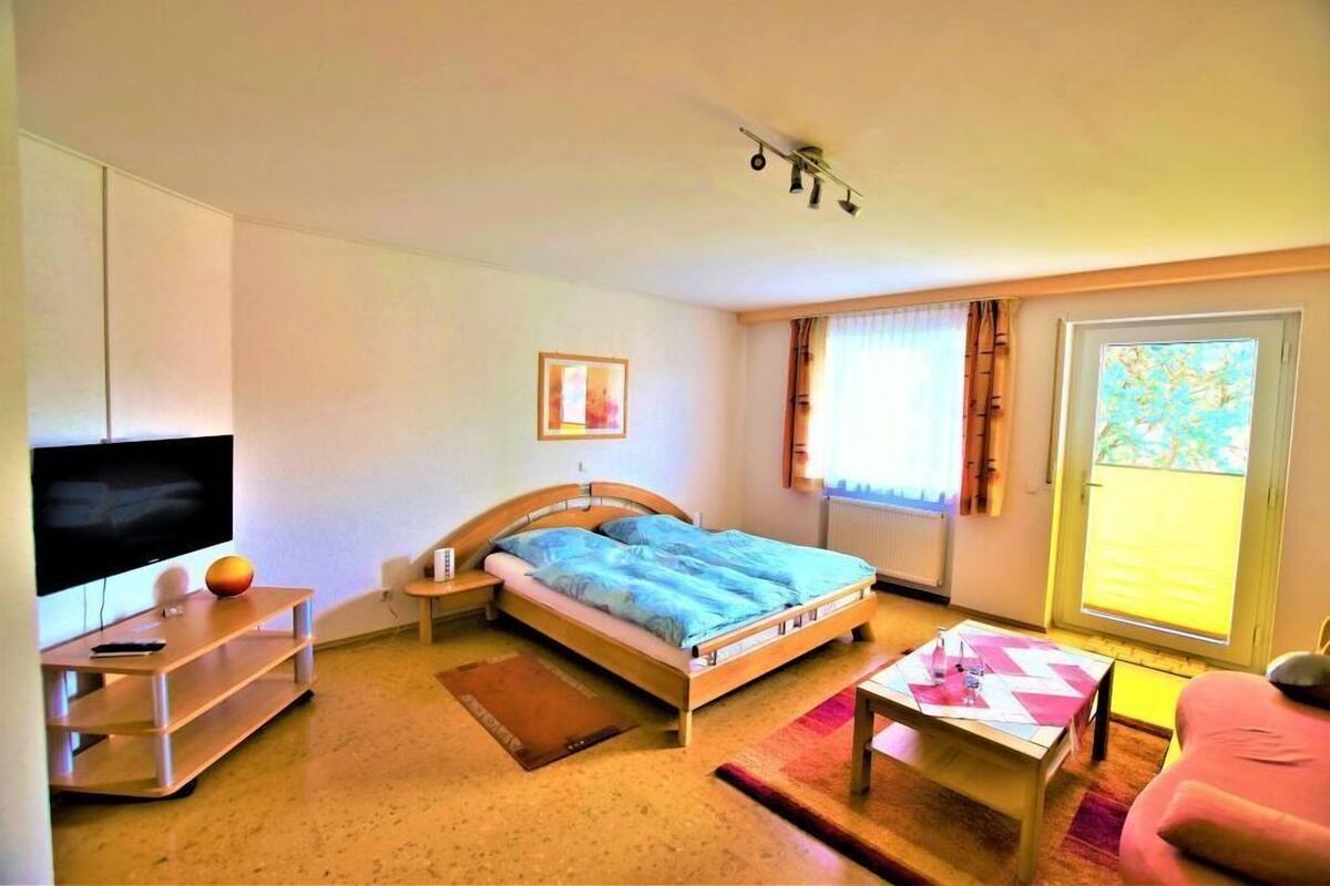 A bedroom with a bed, a TV, a desk, and a window.