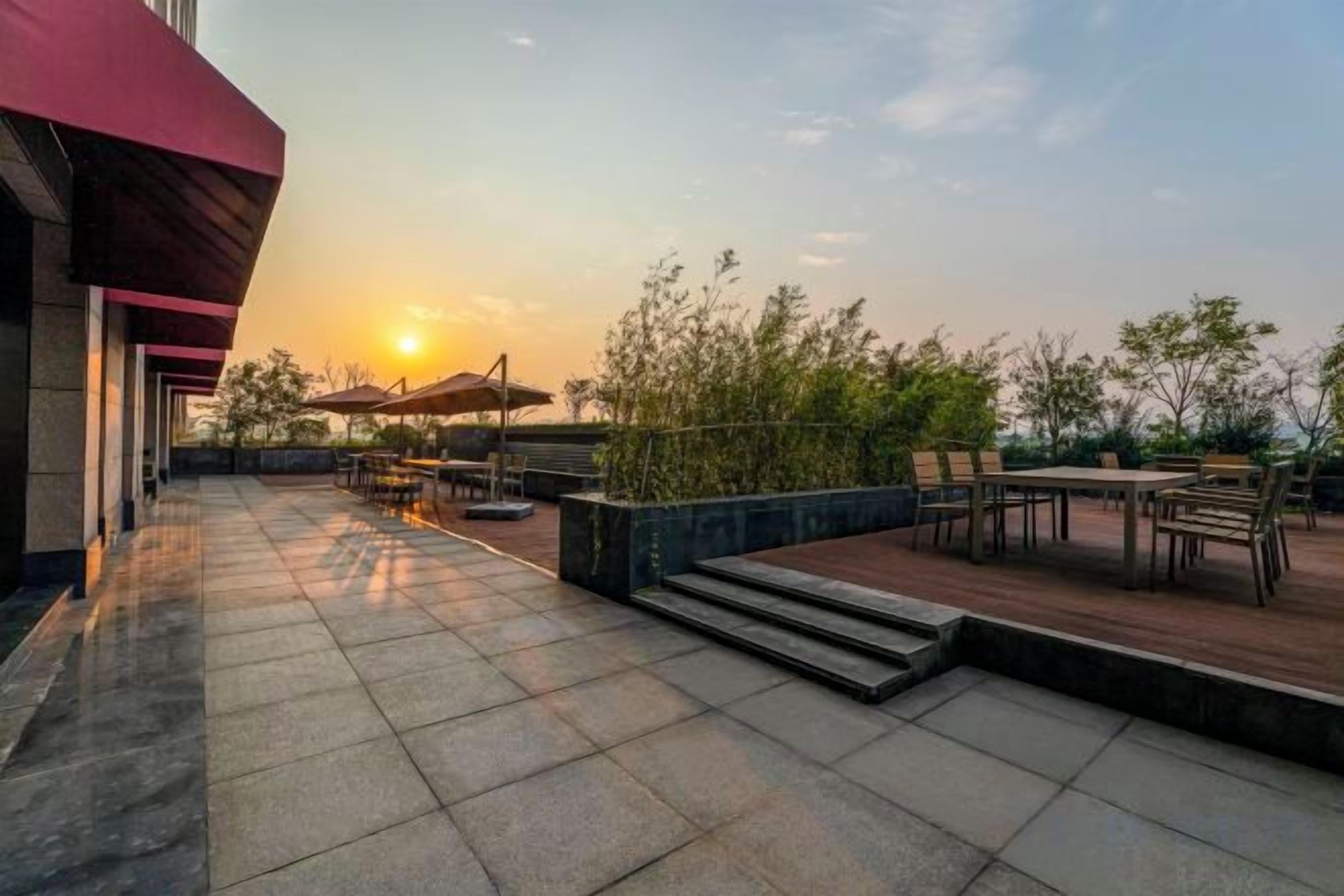 An outdoor patio area with tables and chairs, a red awning, and a view of the sunset.