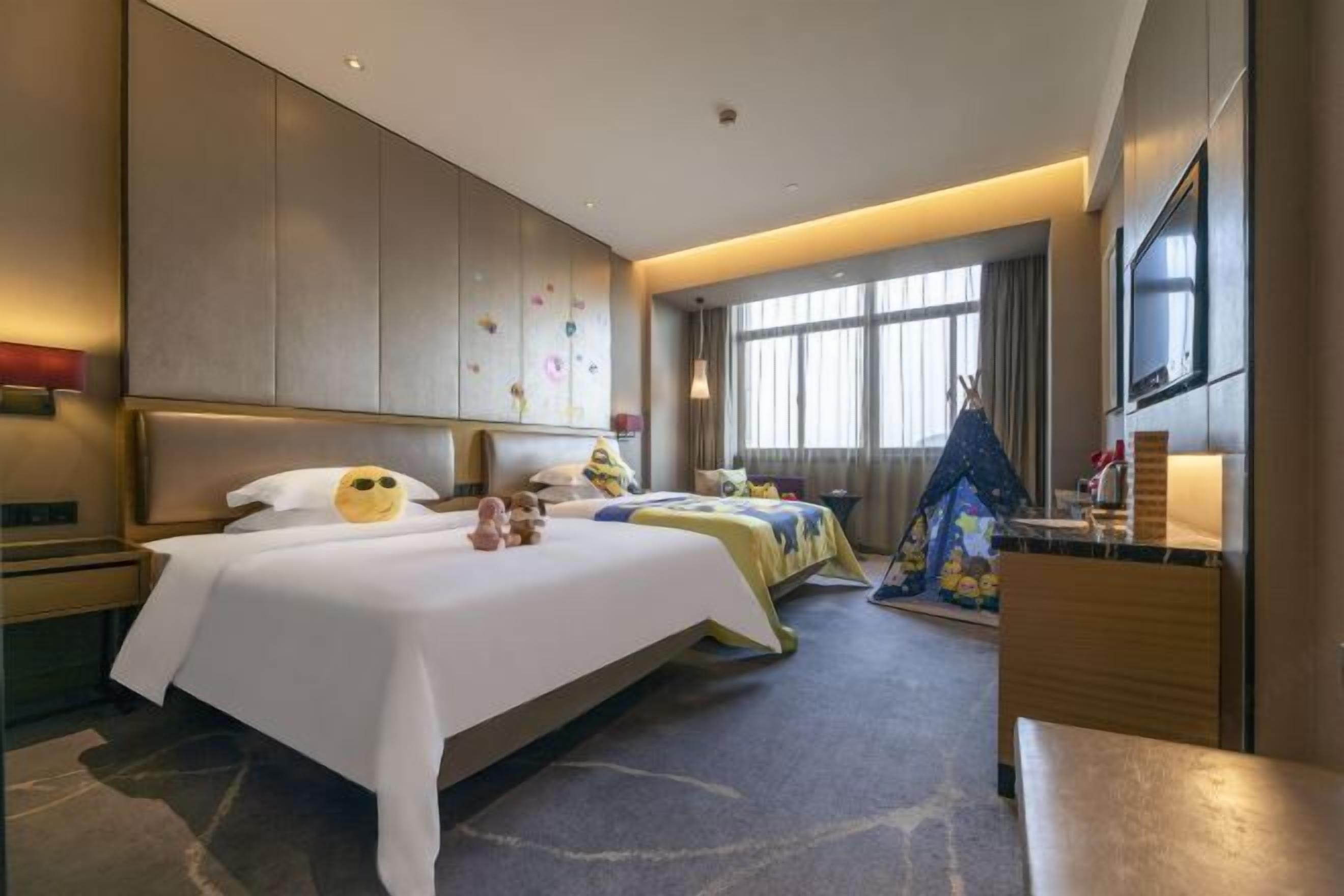 Ein Hotelzimmer mit einem großen Bett, einem kleineren Bett, einem Schreibtisch und einem Fenster mit Vorhängen.