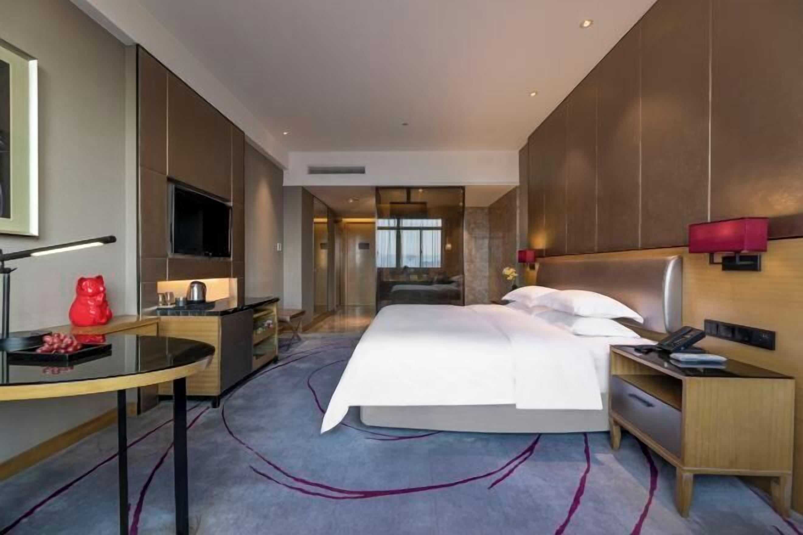 Ein modernes Hotelzimmer mit einem großen Bett, einem Schreibtisch, einem Fernseher und Blick auf die Stadt.