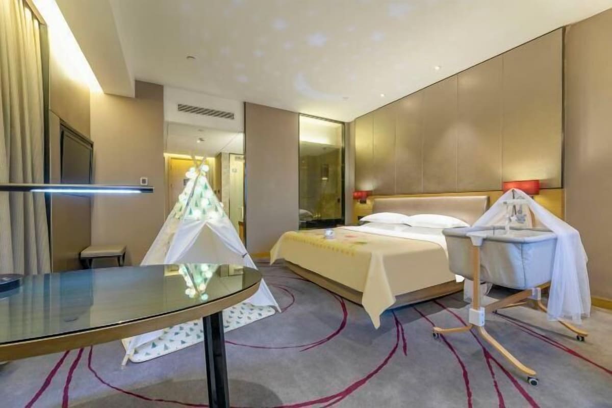 A hotel room with a bed, a glass table, a baby changing station, and a mirror.