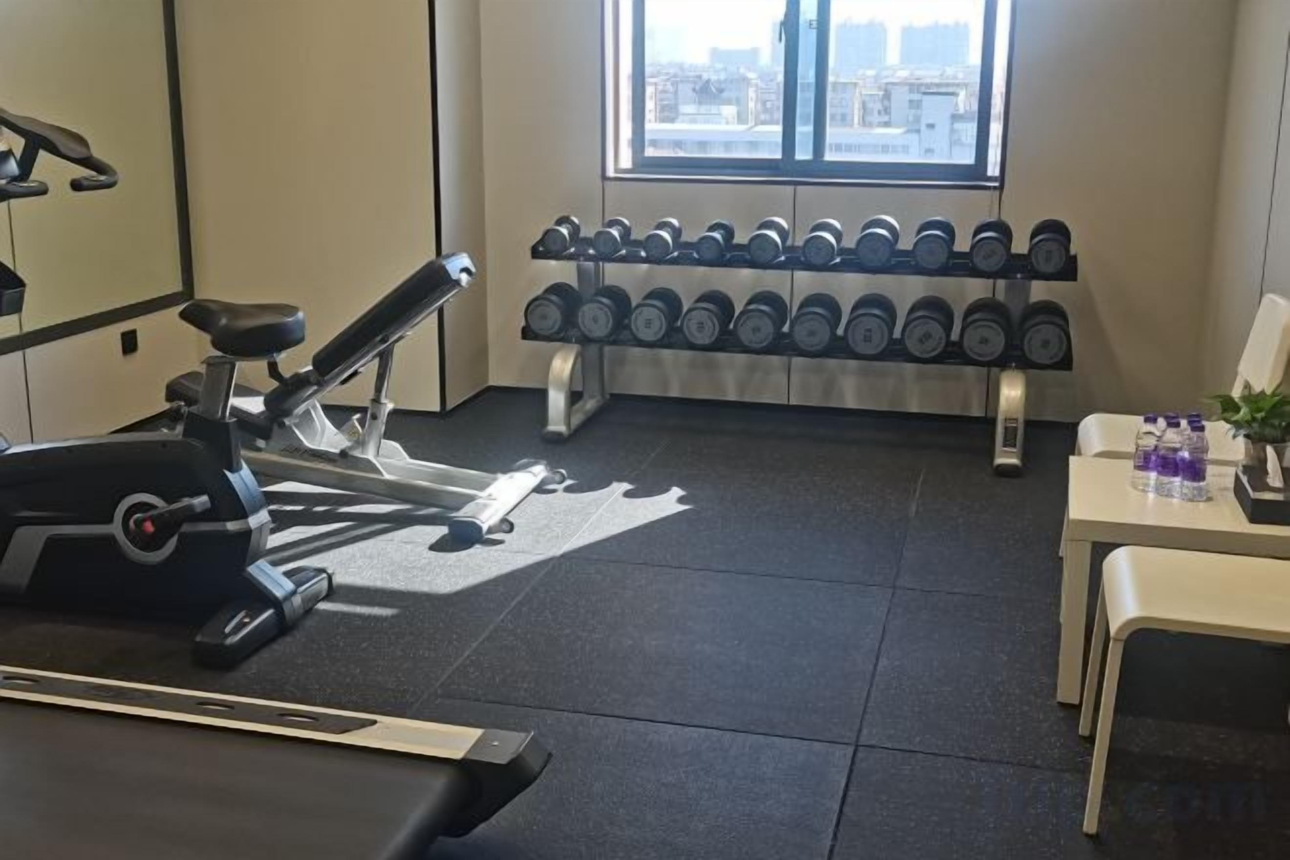 A gym with exercise equipment, dumbbells, and a window with a city view.
