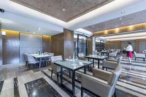 A modern hotel dining area with tables and chairs, a person walking, and a glass partition. - 3b Hotel (Yuyao Shengshan) (Yuyao)