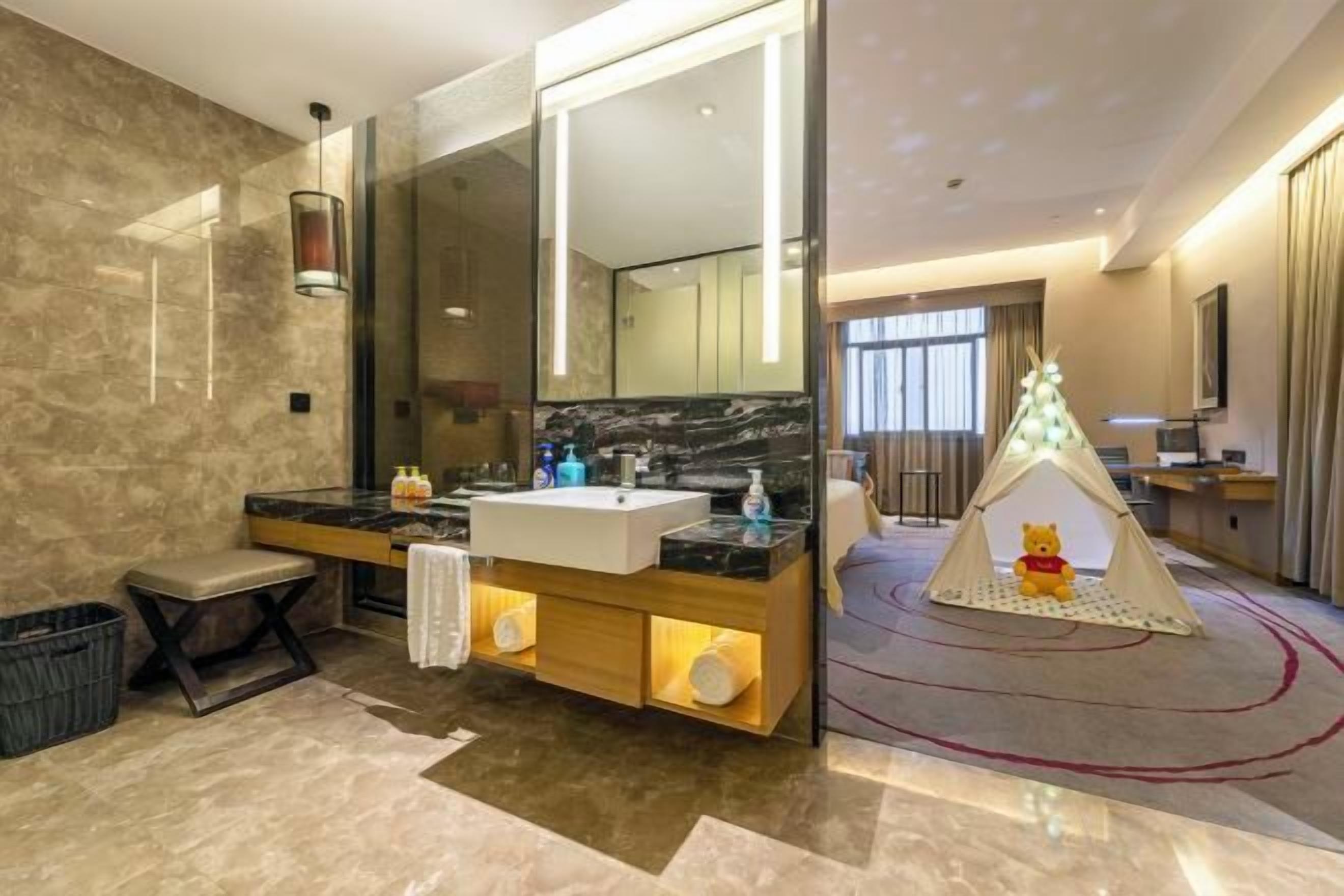 A modern bathroom with a large mirror, dual sinks, and a teddy bear in a tent.