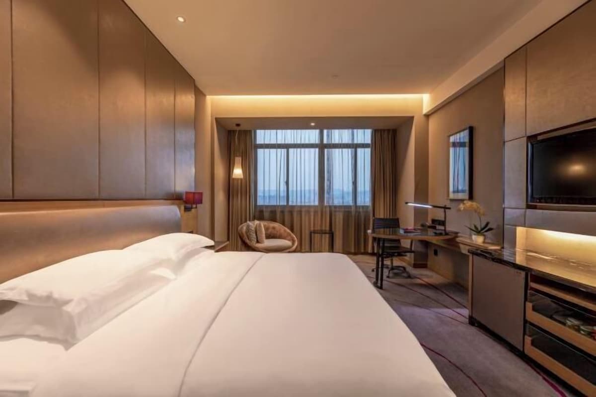 A hotel room with a large bed, a desk, a chair, a TV, and a window with curtains.