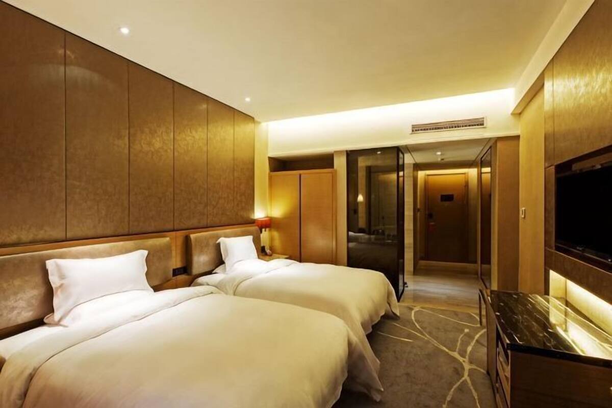 Ein Hotelzimmer mit zwei Betten, einem Fernseher und einem Flur, der zu einem Aufzug führt.