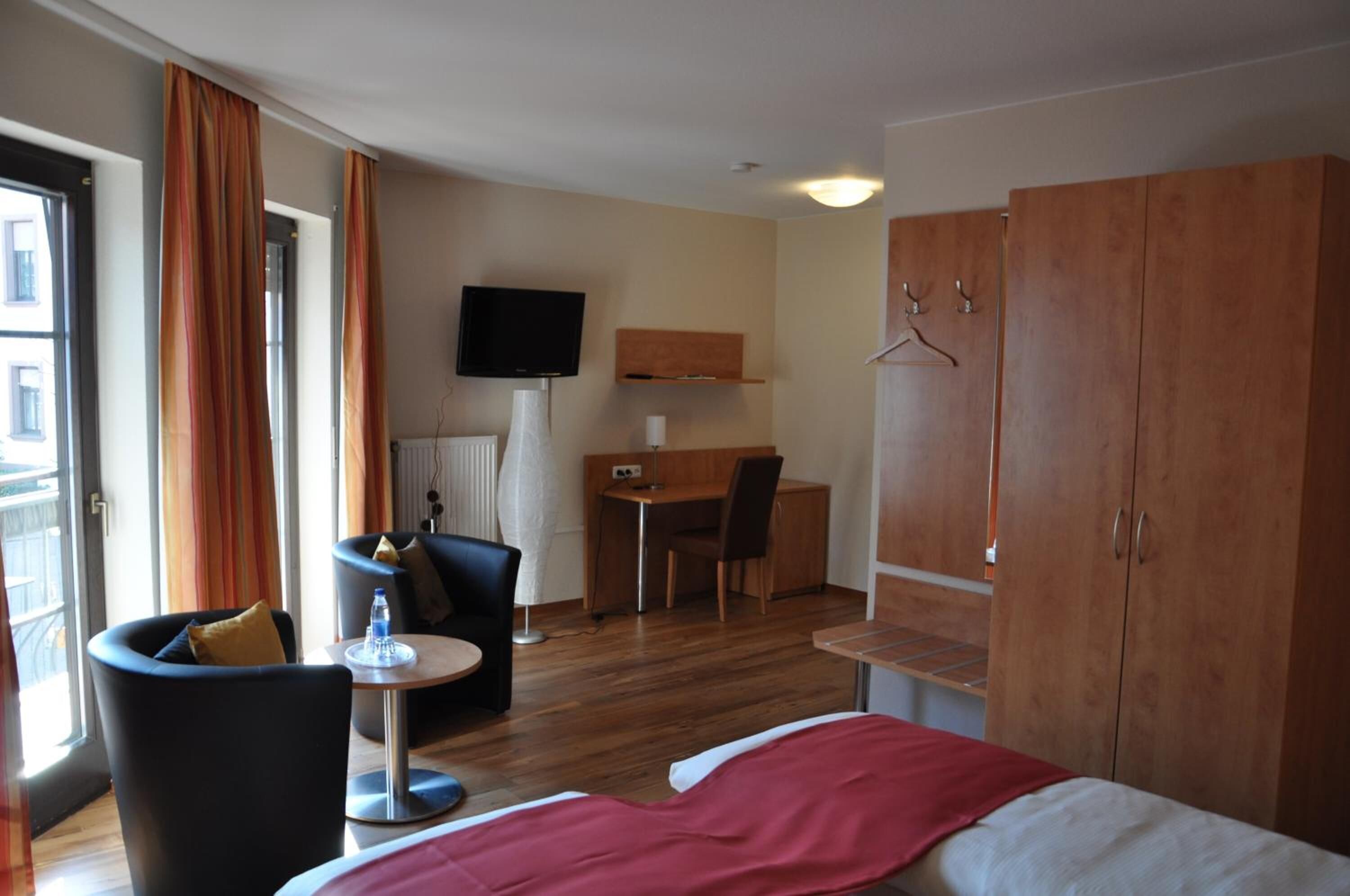 A hotel room with a bed, a desk, a chair, a TV, and a wardrobe.