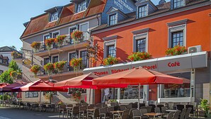 Un café con terraza, sombrillas rojas y macetas con flores en los balcones.