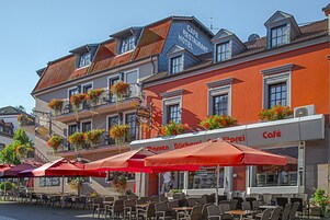 Un café con terraza, sombrillas rojas y macetas con flores en los balcones.