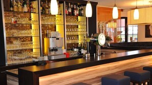Una zona de bar con estanterías llenas de copas y botellas, una barra y taburetes azules.