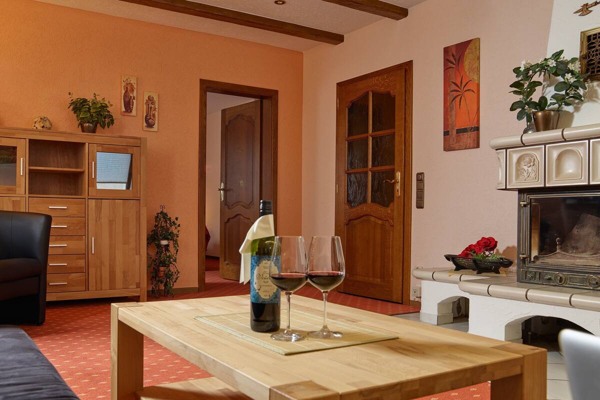 A cozy living room with a fireplace, wooden furniture, and a dining table with wine glasses.
