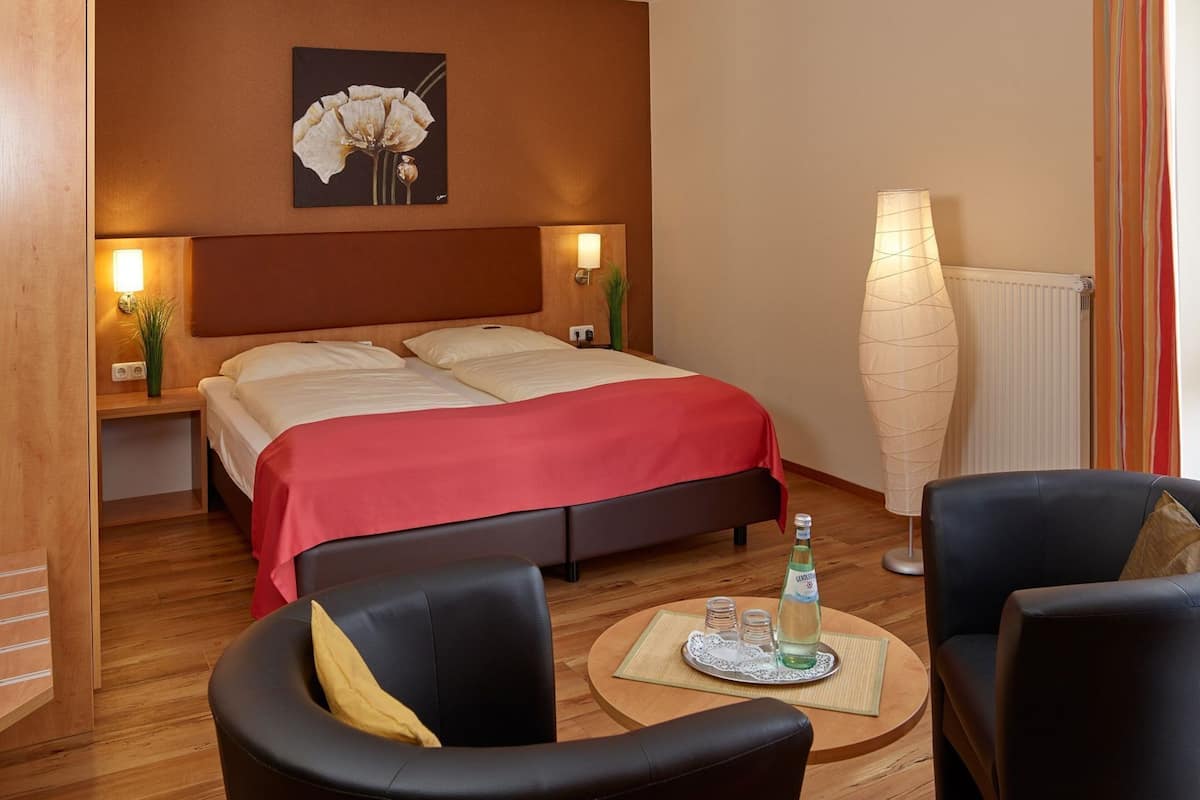 A hotel room with a double bed, two bedside tables with lamps, a large vase, and two armchairs.