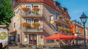 Un edificio tradicional europeo con mesas al aire libre y jardineras con flores en los balcones.