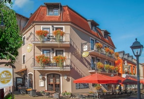 Un edificio tradicional europeo con mesas al aire libre y jardineras con flores en los balcones.