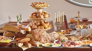 Una mesa de buffet con panes, pasteles, quesos, carnes y frutas variadas.