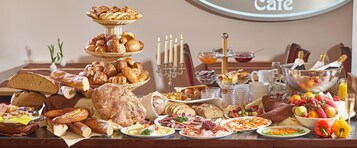 Una mesa de buffet con panes, pasteles, quesos, carnes y frutas variadas.
