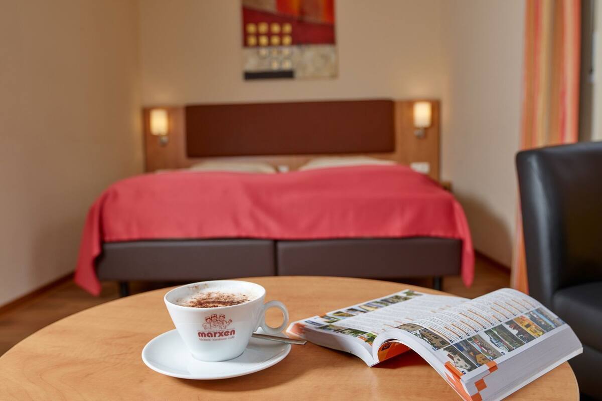 A hotel room with a bed, a coffee cup, and a magazine on a table.