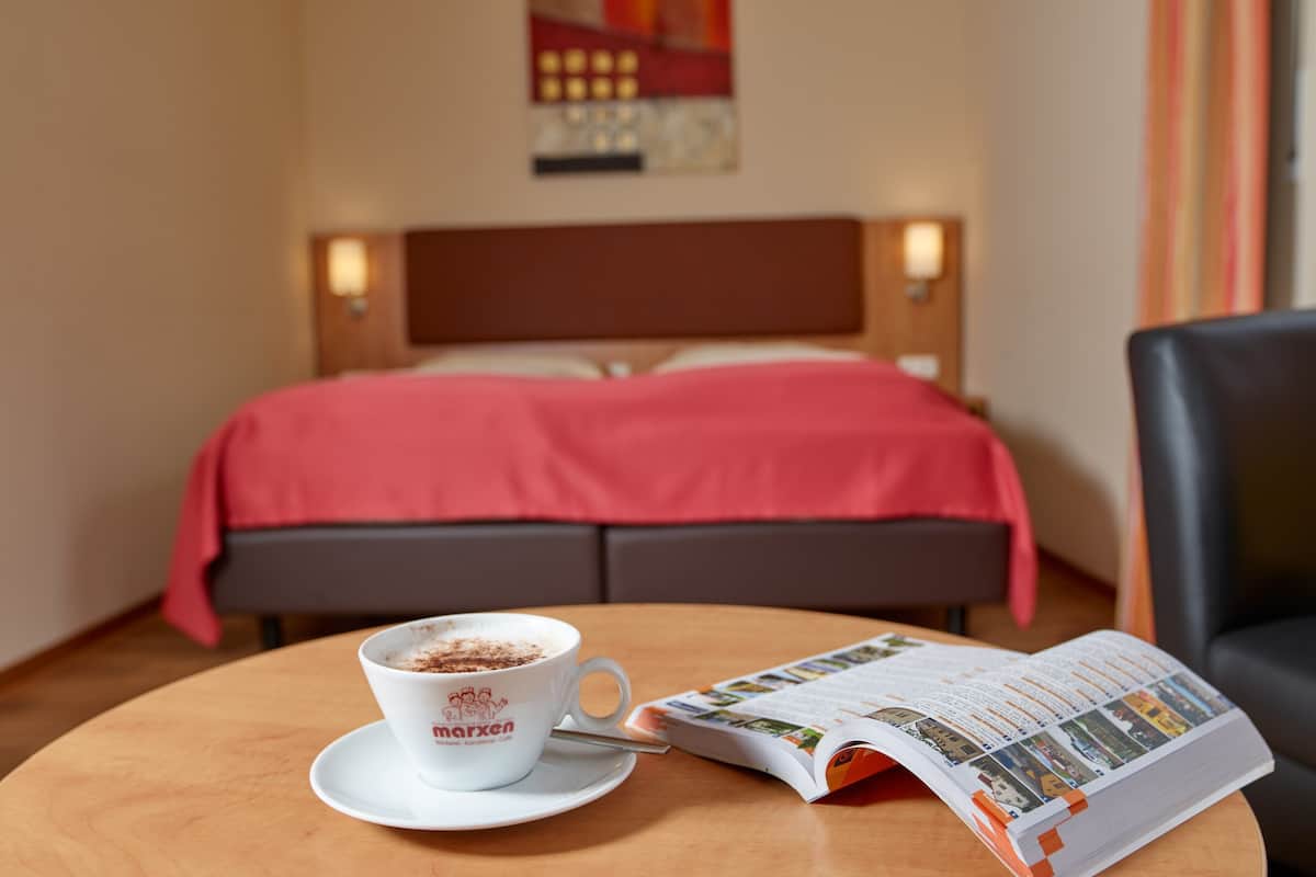 A hotel room with a bed, a coffee cup on a table, and a magazine.