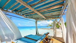 A wooden deck with two lounge chairs, a covered area with a blue mesh roof, and a view of the ocean. - Hotel Isla Palma (Isla Palma)